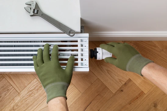 Local technique moderne avec chaudière murale blanche, ballon d'eau chaude vertical en inox, circuit de distribution avec collecteur à vannes rouges et tubes noirs isolés
